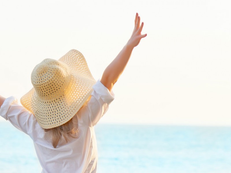 woman wearing sunhat throwing hands in air